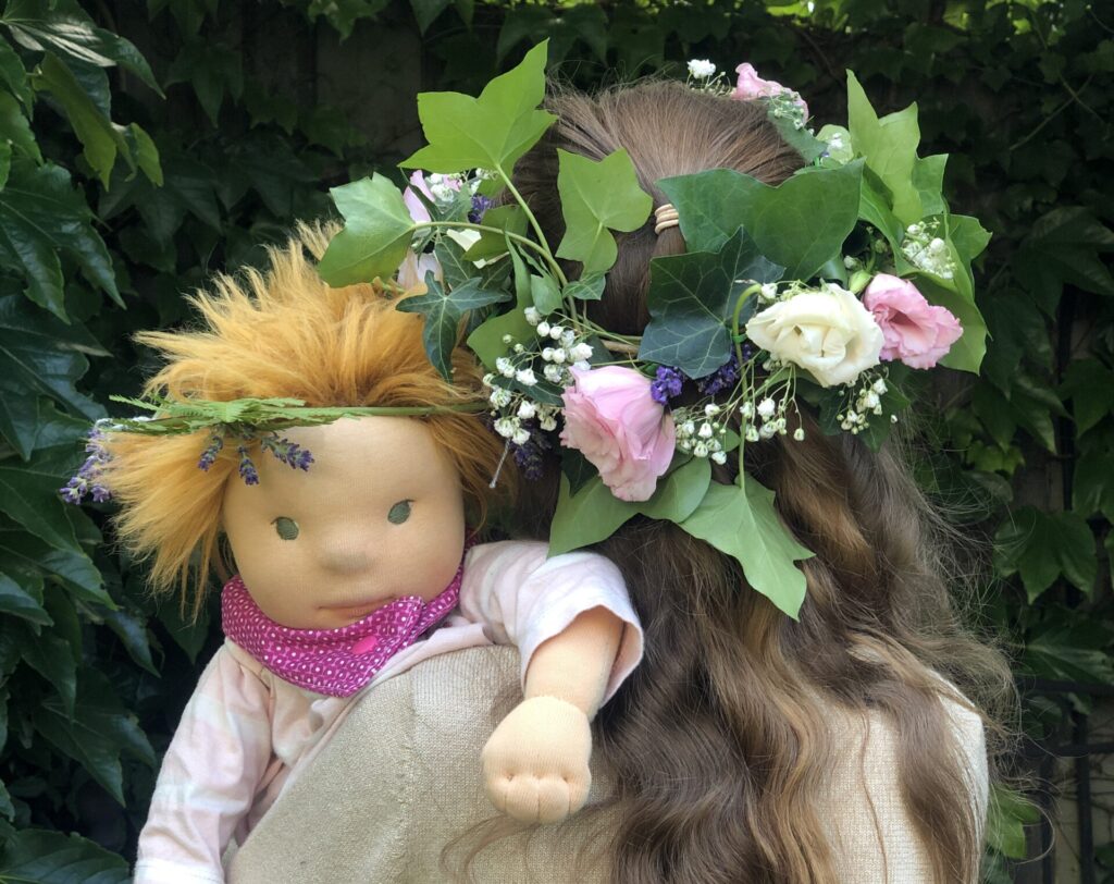 Kind mit Blumenkranz und Waldorfpuppe auf dem Arm